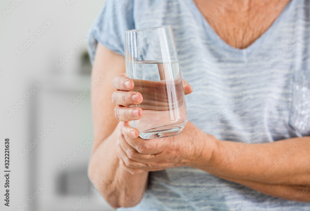 Senior woman suffering from Parkinson syndrome with glass of water in clinic, closeup Senior woman suffering from Parkinson syndrome with glass of water in clinic, closeup