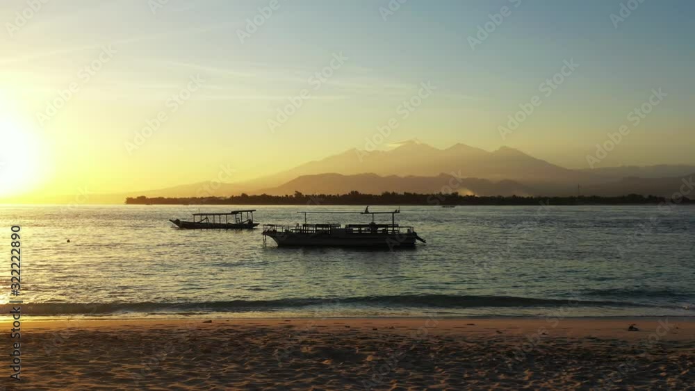 Silhouette of anchored boats on calm bay with sea surface reflecting yellow sun setting down the horizon of tropical islands in Bali Silhouette of anchored boats on calm bay with sea surface reflecting yellow sun setting down the horizon of tropical islands in Bali