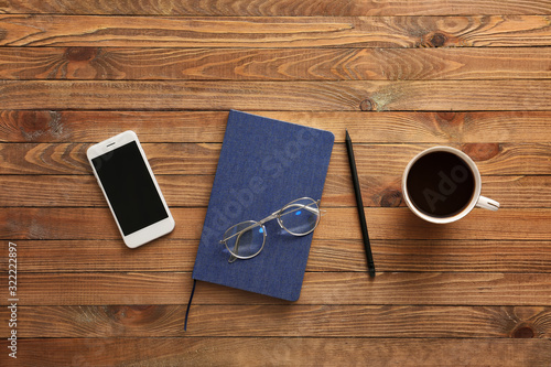 Notebook with mobile phone, cup of coffee and eyeglasses on wooden table