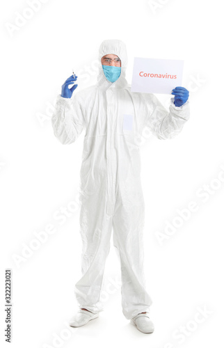 Laboratory worker in protective uniform holding syringe and paper with text CORONAVIRUS on white background. Concept of epidemic