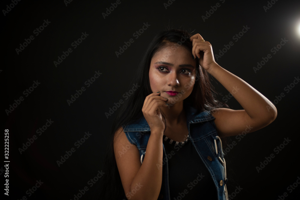 Fashion portrait of an young and attractive Indian Bengali brunette girl with tee shirt and blue western jacket in front of a black studio background. Indian fashion portrait and lifestyle.