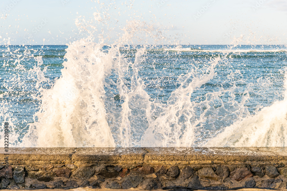 Obraz premium Close up of a stone wall where waves are crashing over, at the ocean, at Waikiki Beach in Honolulu, Hawaii.