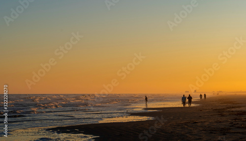 Tranquil beach scene at Port Aransas, Texas at sunset with waves, clear sky and silhouette of a few people. © scandamerican