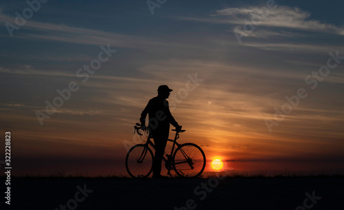 Cyclist standing next to bike, alone at sunset in natural setting
