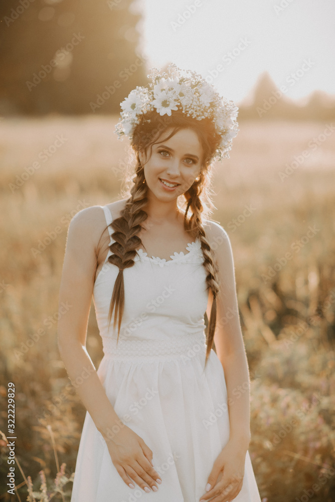 portrait of smiling girl in white dress with floral wreath and braids in summer at sunset in the field portrait of smiling girl in white dress with floral wreath and braids in summer at sunset in the field