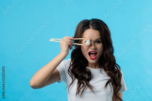 Portrait of a brunette girl who has hadi sushi in her hands. The girl opened her mouth wide in surprise. She brought sushi to her eye photo