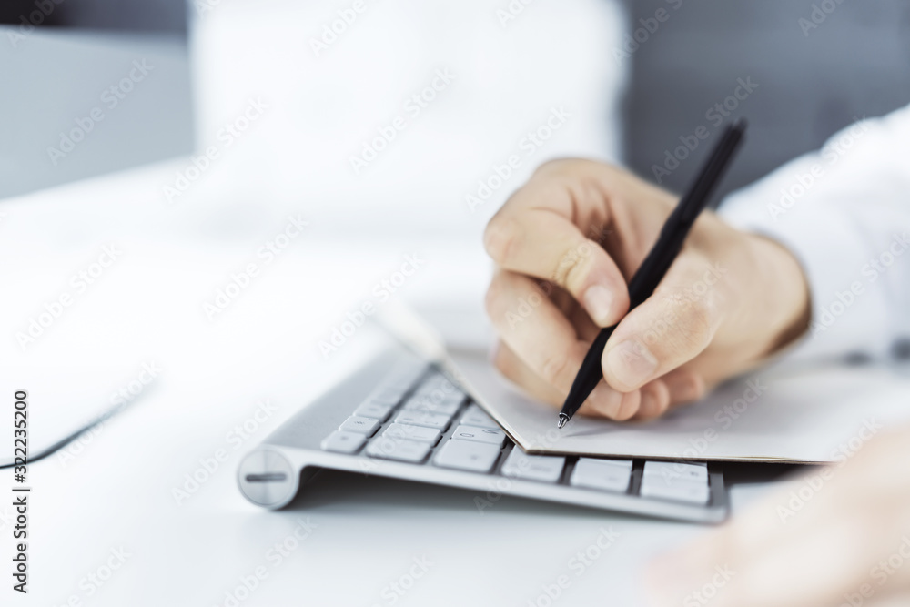 Closeup of man hand writing in diary on a table with computer. Focused on a pen. Close up Closeup of man hand writing in diary on a table with computer. Focused on a pen. Close up