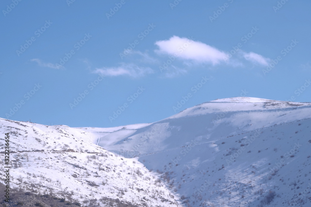 Obraz premium A beautyfool panoramic view of snowy mountain. Dramatic clouds. Trees in the Shed. blue sky. Mt hermon the higher mountain in Israel.