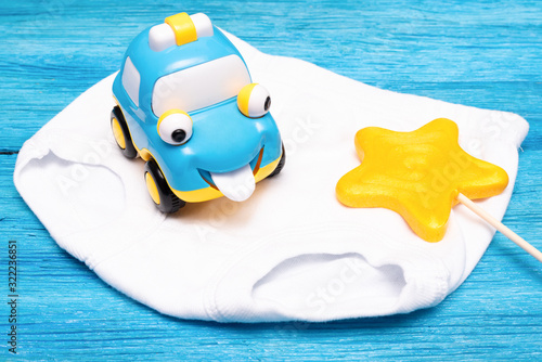 Yellow star shape lollipop, toy car and white children pants close up over blue wooden background. © Natali