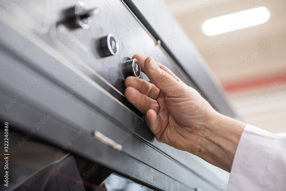 Close-up of unrecognizable man pushing button with arrow down while using automated factory machine