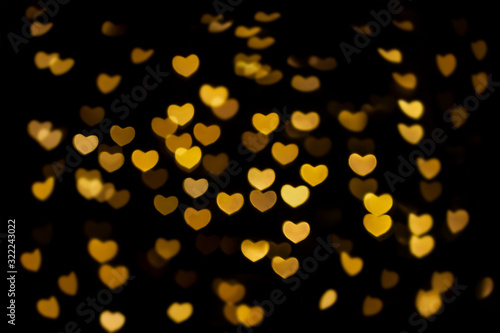 Abstract beautiful romantic picture of blur bright Gold-Yellow colored of swirl heart shaped bokeh on black from ornamental lights flickering. Background for Valentine’s day or Love or Romance concept
