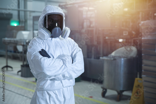 man in chemical protection clothes and toned mask in a factory against the background of an industrial workshop looking into the frame.  photo