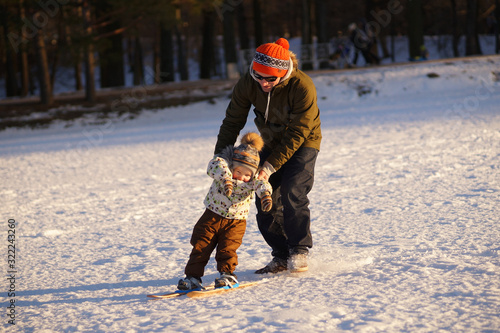 Young man learning his small child how to ski. Sunny photo on background of winter snowy park