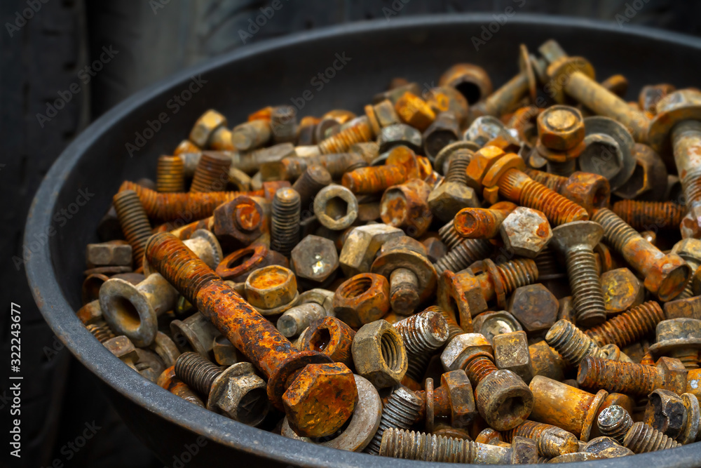 Fototapeta premium Group of unused old rusty steel nuts and bolts from machine and vehicles pile in a black bowl in recycle factory. Background for garbage and waste in reuse industry or the environment problem concept.