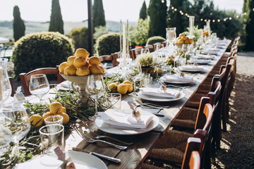 in the back yard of the old villa there is a long festive table, which is decorated with lemons and herbs, on the table are plates, glasses and candles. Wedding in Italy. Tuscany