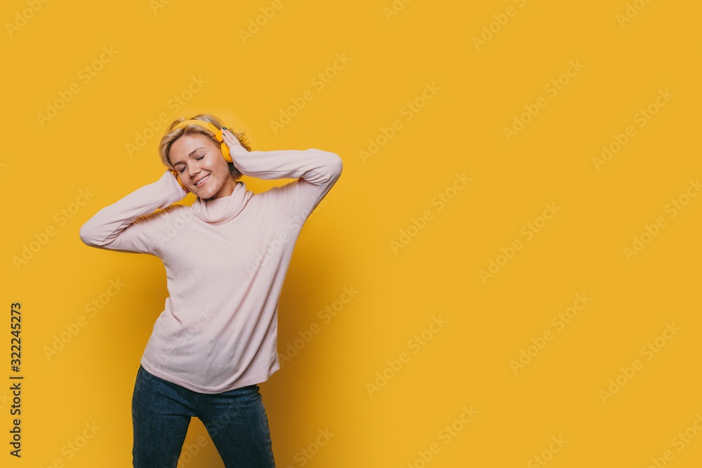 The picture of a happy and joyful student who is advertising something by listening to music near a yellow blank space The picture of a happy and joyful student who is advertising something by listening to music near a yellow blank space