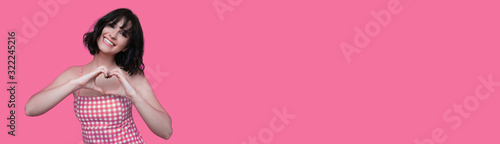 A wonderful lady dressed in pink , smiling on a pink blank space background , showing love for something