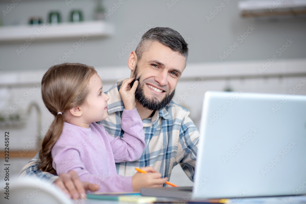 Dad with daughter in her arms sitting in front of laptop. Dad with daughter in her arms sitting in front of laptop.