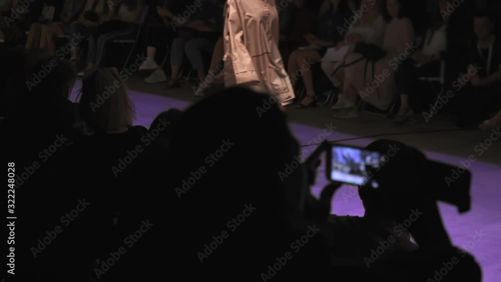 fashion show of brand new collection of modern clothing, slender unrecognizable model walks along purple path, viewers shoot videos on mobile devices and phones fashion show of brand new collection of modern clothing, slender unrecognizable model walks along purple path, viewers shoot videos on mobile devices and phones