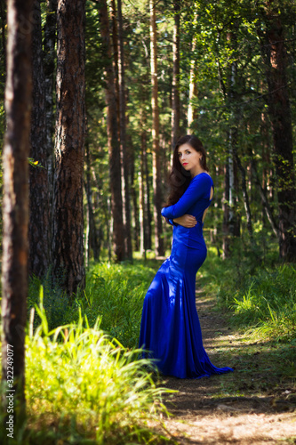 Beautiful, young girl dressed in a blue dress, on a background of a pine forest.