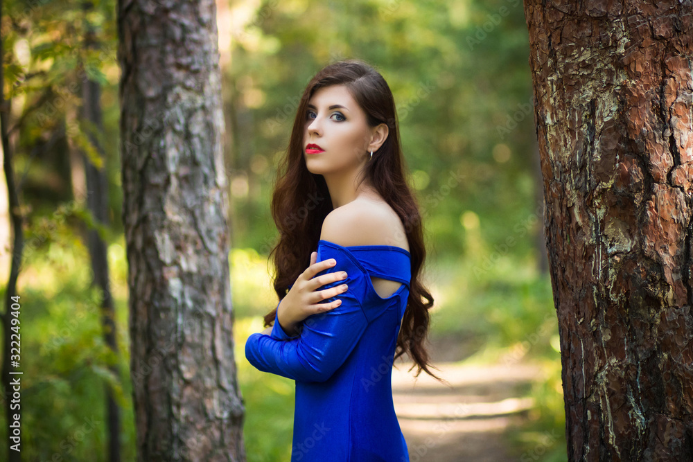 Portrait of a beautiful, young girl in a blue dress against a forest background.