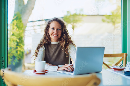 Attractive young curly brunette enjoying her coffee and working on laptop  © Tijana