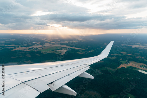Wing of a flying airplane on clouds, view from the airplane window at sunset