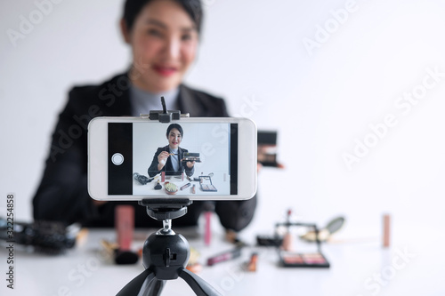 Business online on social media, Beautiful woman blogger is showing present tutorial beauty cosmetic product and broadcast live streaming video to social network while recording teaching online © Ngampol