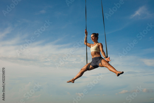 aerial yoga meditation workout  isolated on blue sky - young attractive and healthy woman practicing aero-yoga training balance body and mind control hanging from ropes
