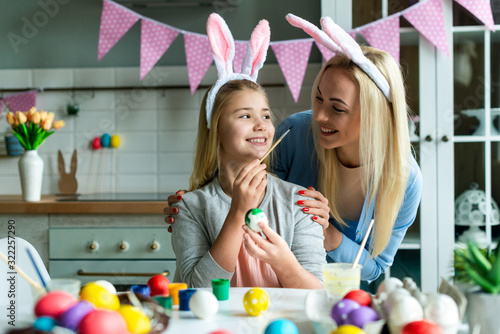 Happy holiday! A mother and her daughter are painting eggs. Family preparing for Easter. Cute little child girl is wearing bunny ears.