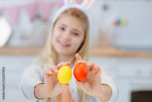 Young, cute girl in bunny earsshowing a hand-made eggs. Easter traditions.