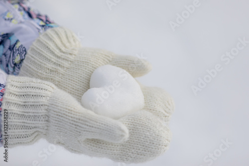 Valentine day background. Female hands in knitted mittens with heart of snow in winter day. Love concept. 
