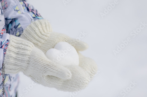 Valentine day background. Female hands in knitted mittens with heart of snow in winter day. Love concept. 