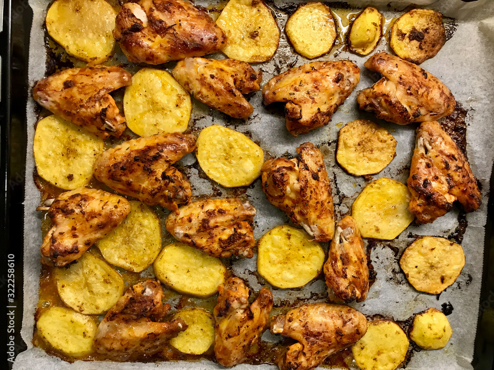 Marinated and Baked Chicken Wings with Potatoes on Baking Tray with Oven Sheet Paper. Marinated and Baked Chicken Wings with Potatoes on Baking Tray with Oven Sheet Paper.