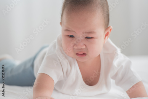 newborn child crying in bed. adorable baby boy in white sunny bedroom. nursery for young children. textile and bedding for kids. family morning at home. fussy baby. childhood and baby care concept