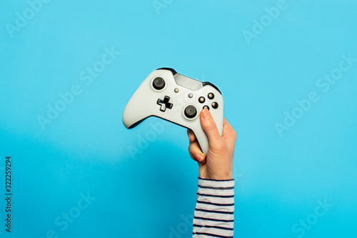 Female hand hold a gamepad on a blue background. Concept of the game, e-sports, leisure, gaming industry, video games. Banner. Flat lay, top view