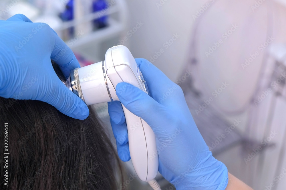 Doctor trichologist examines woman patient's hairs using trichoscope in