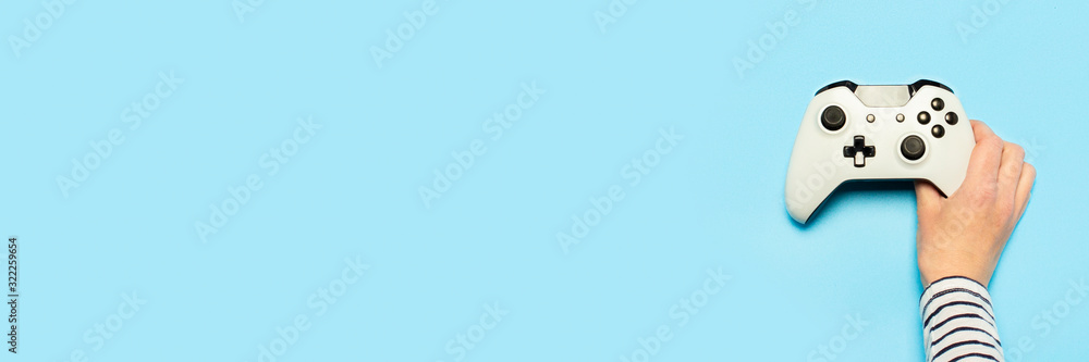 Female hand hold a gamepad on a blue background. Concept of the game, e-sports, leisure, gaming industry, video games. Banner. Flat lay, top view Female hand hold a gamepad on a blue background. Concept of the game, e-sports, leisure, gaming industry, video games. Banner. Flat lay, top view