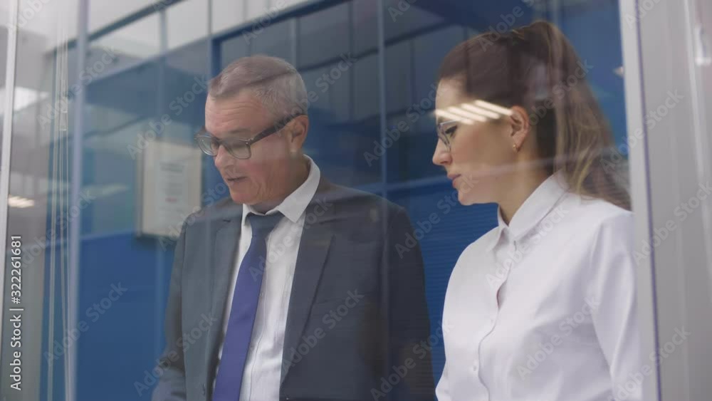 Businessman talks to his younger female assistant. Office colleagues communicate. View through transparent glass window Businessman talks to his younger female assistant. Office colleagues communicate. View through transparent glass window