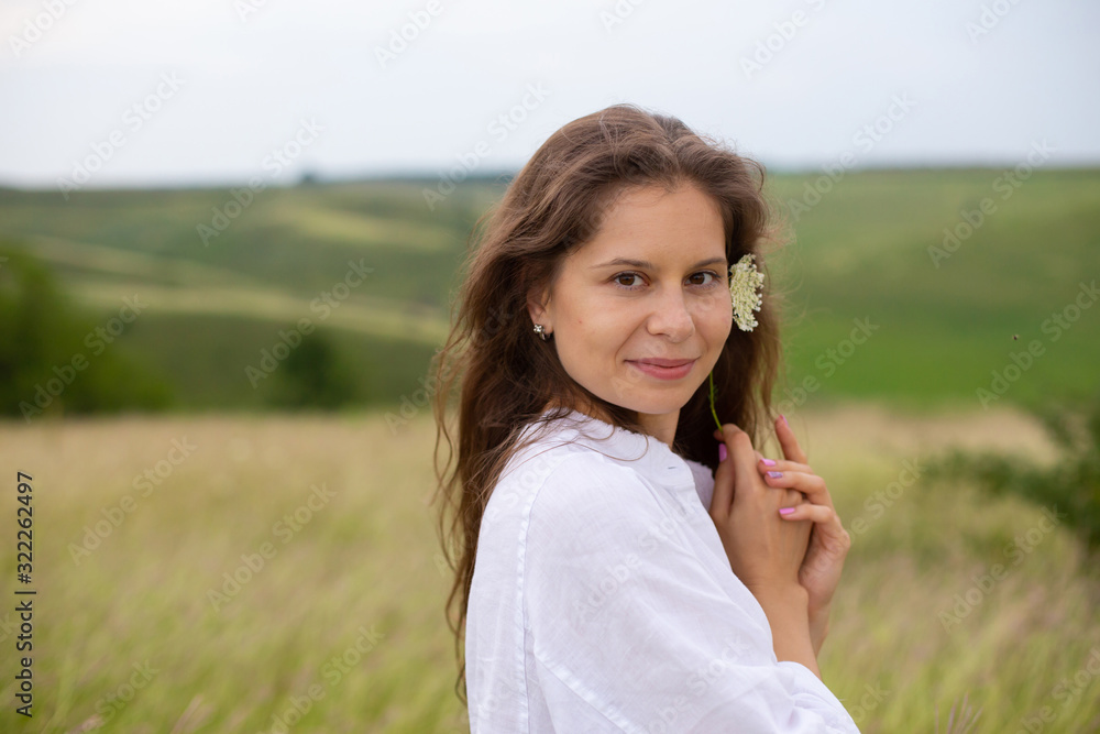 horizontal photo of a young european woman who stands in a field with a flower in her hands