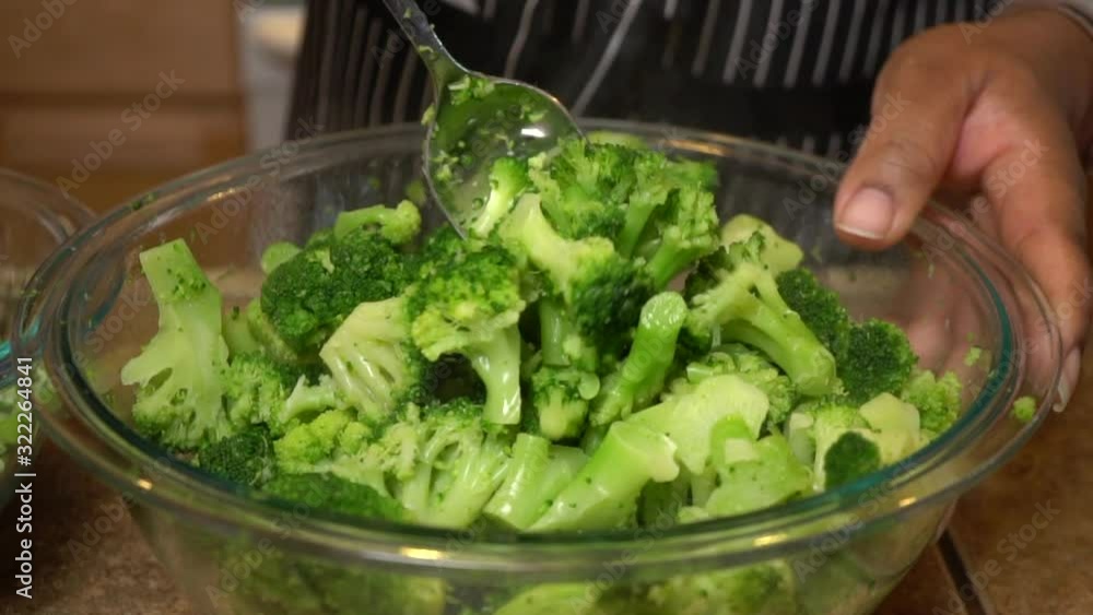 Cook stirs steamed broccoli in glass bowl with tablespoon, slow motion Cook stirs steamed broccoli in glass bowl with tablespoon, slow motion