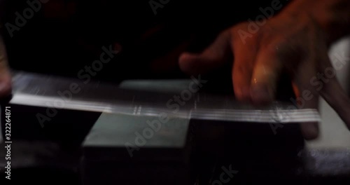 Professional craftsman sharpening Taiwan made Japanese knife blade on wet stone block close up.