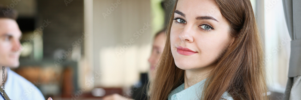 Fototapeta premium Beautiful smiling cheerful girl at cafe look in camera with colleagues group in background. White collar worker at workspace job offer modern lifestyle client visit profession train concept