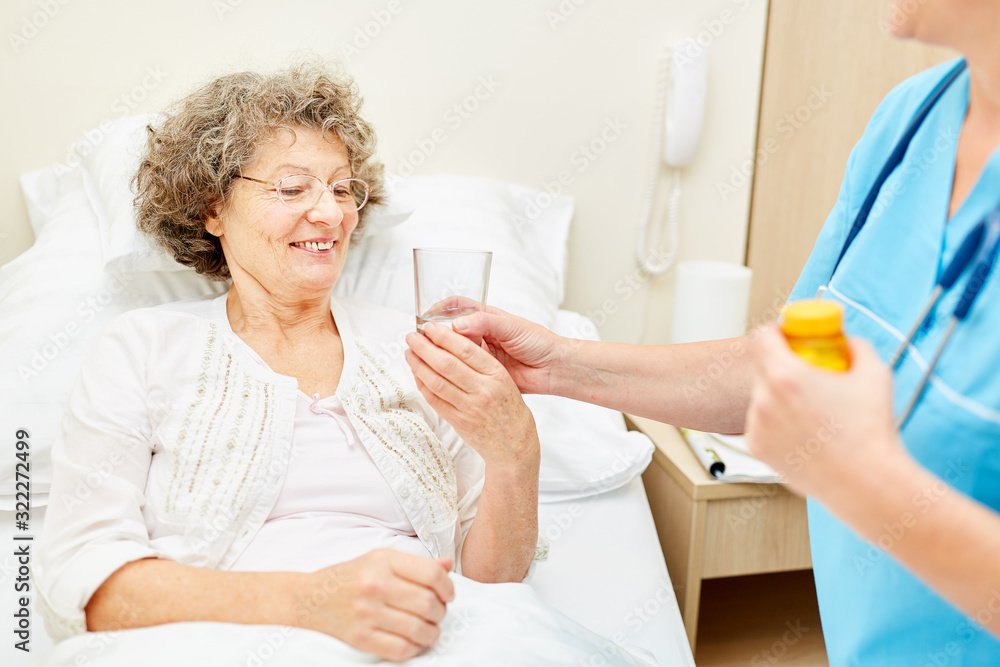 Fototapeta premium Caregiver gives tablets to old woman