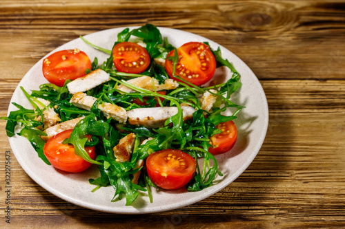Tasty salad of fried chicken breast, fresh arugula and cherry tomatoes on wooden table