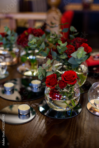 vertical photo of a wooden dining table decorated with bouquets of roses and candles