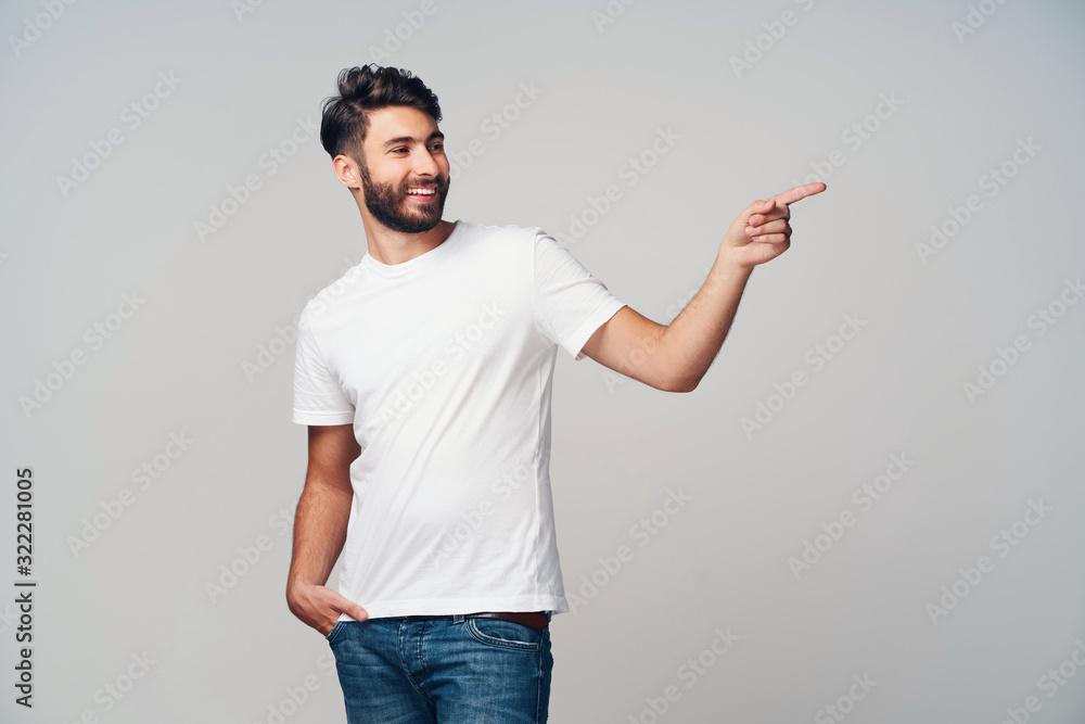 Handsome young man pointing isolated on grey background wearing casual t-shirt and jeans Handsome young man pointing isolated on grey background wearing casual t-shirt and jeans