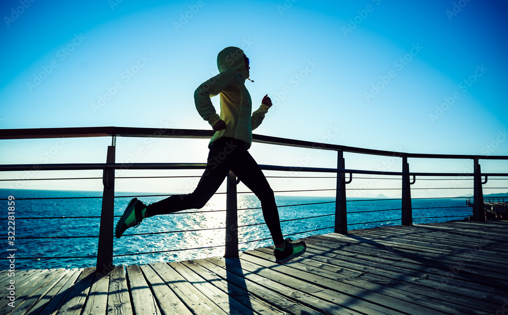 Sporty female jogger morning exercise on seaside boardwalk during sunrise