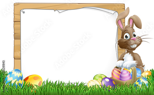 Easter bunny rabbit peeking around a sign and pointing with Easter eggs and basket background cartoon