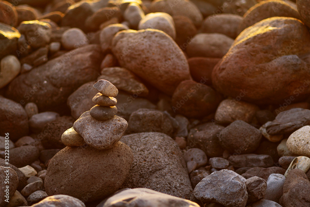 Balanced stone pyramide on shore of the ocean at dawn. Sea pebbles tower closeup symbolizing stability, zen, harmony, balance.